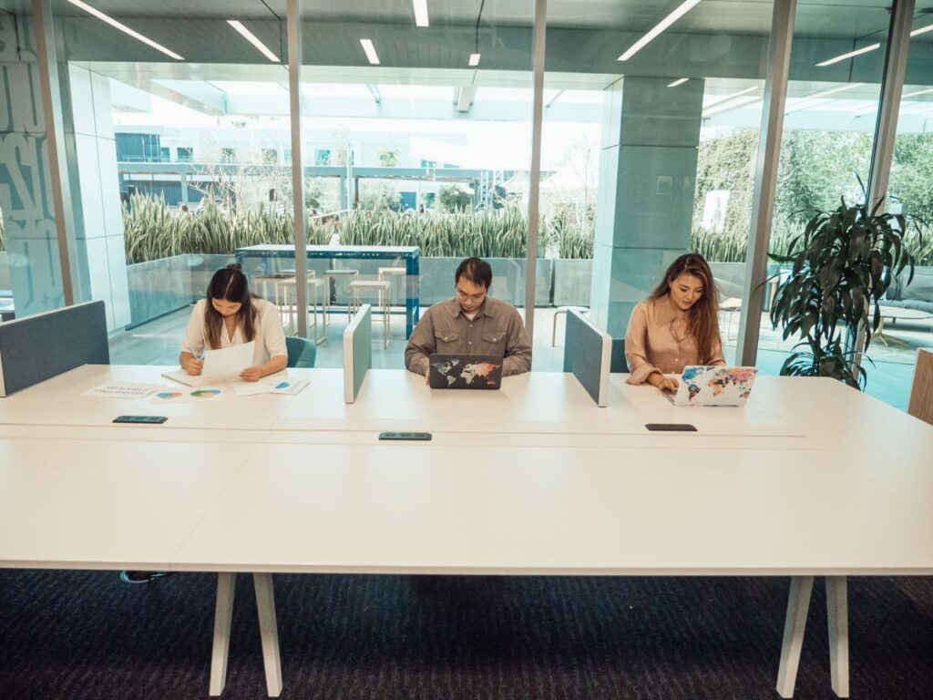 Three professionals collaborating in a modern office space with laptops and documents.